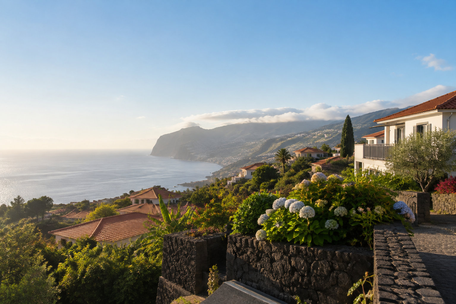 Quartiers résidentiels paisibles à Madère Vue panoramique sur la côte de Madère avec des maisons, des jardins fleuris et l'océan Atlantique au soleil couchant.