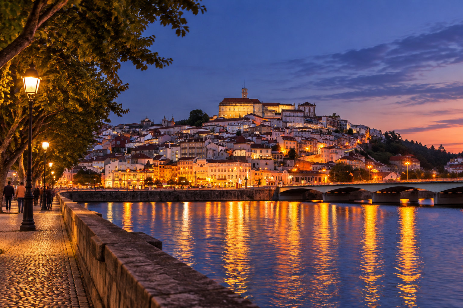 Une ville aux maisons éclairées s’étage sur une colline au bord d’une rivière, traversée par un pont, tandis que des passants marchent sur une promenade au crépuscule.