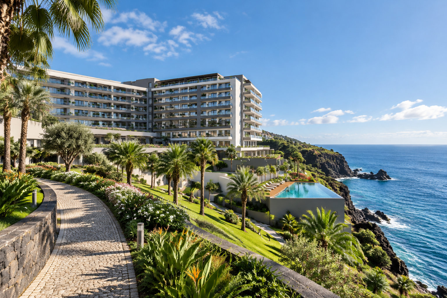 Un grand hôtel moderne entouré de jardins tropicaux et de palmiers surplombe une piscine et une côte rocheuse au bord de la mer.
